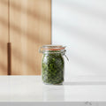 A Kilner round clip top jar made of clear glass with a dark red oval label and metal wire clamp lid, shown on a white background.