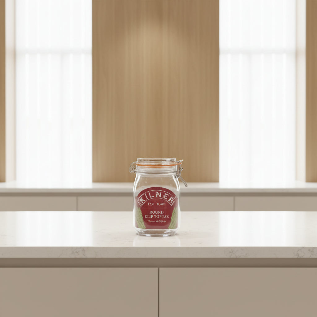 A Kilner round clip top jar made of clear glass with a dark red oval label and metal wire clamp lid, shown on a white background.