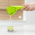 Green hand juicer being used to extract juice into a glass on a white background