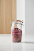 A Kilner round clip top jar made of clear glass with a dark red rubber seal and a metal wire clamp lid, featuring a printed red label with the Kilner brand name and a beet illustration.