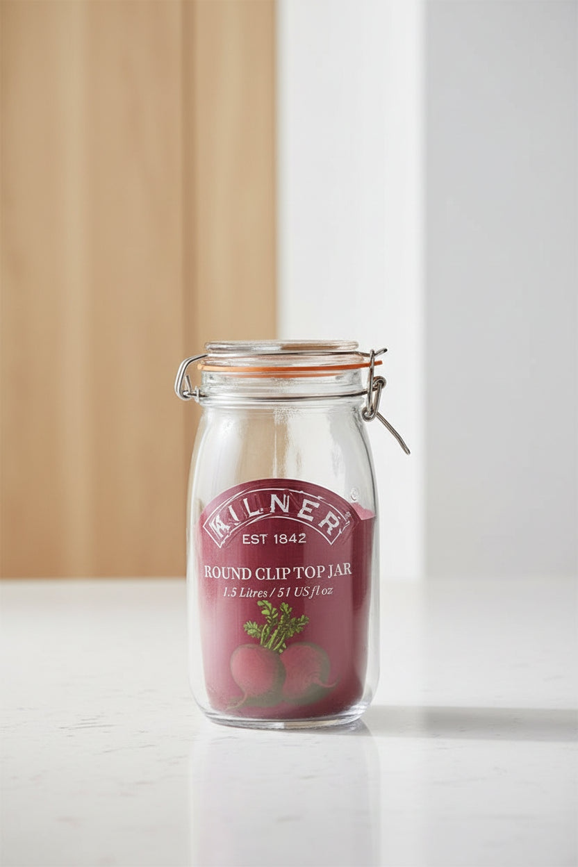A Kilner round clip top jar made of clear glass with a dark red rubber seal and a metal wire clamp lid, featuring a printed red label with the Kilner brand name and a beet illustration.