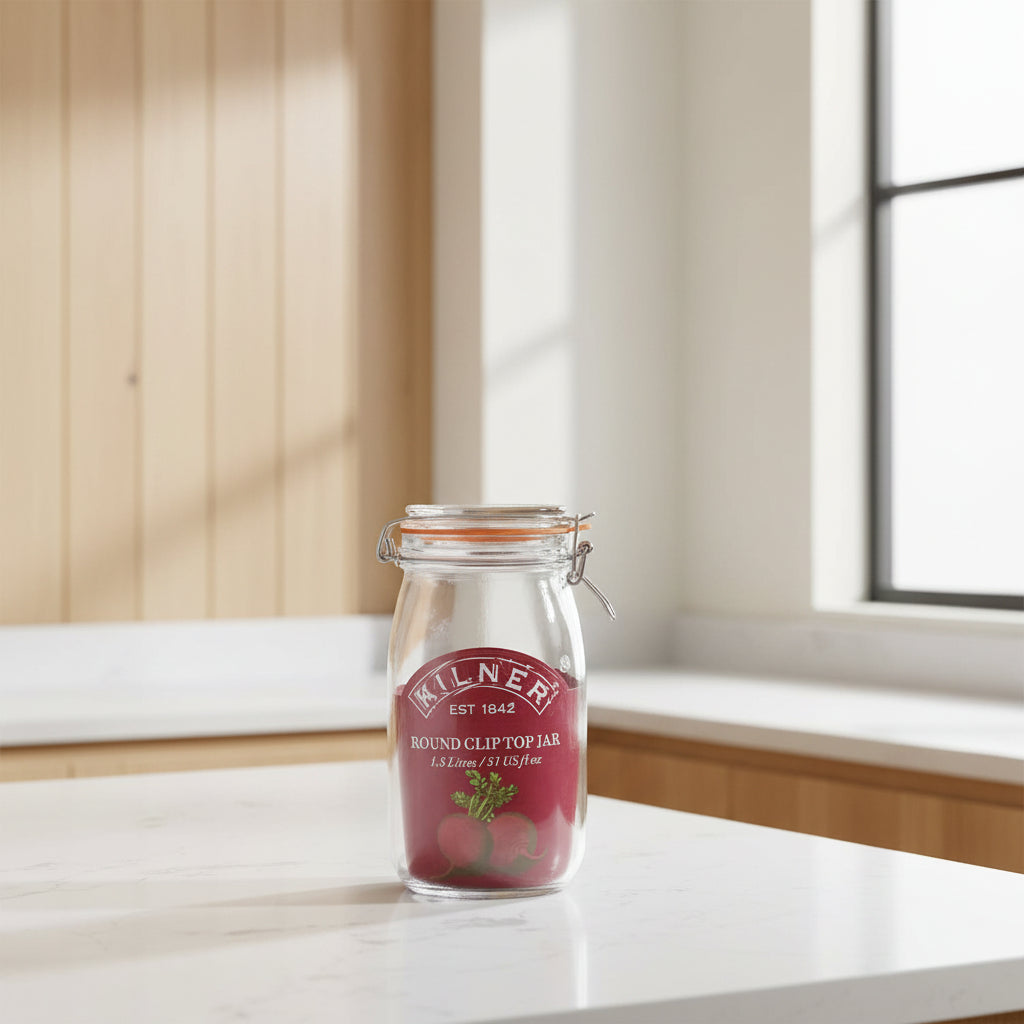 A Kilner round clip top jar made of clear glass with a dark red rubber seal and a metal wire clamp lid, featuring a printed red label with the Kilner brand name and a beet illustration.