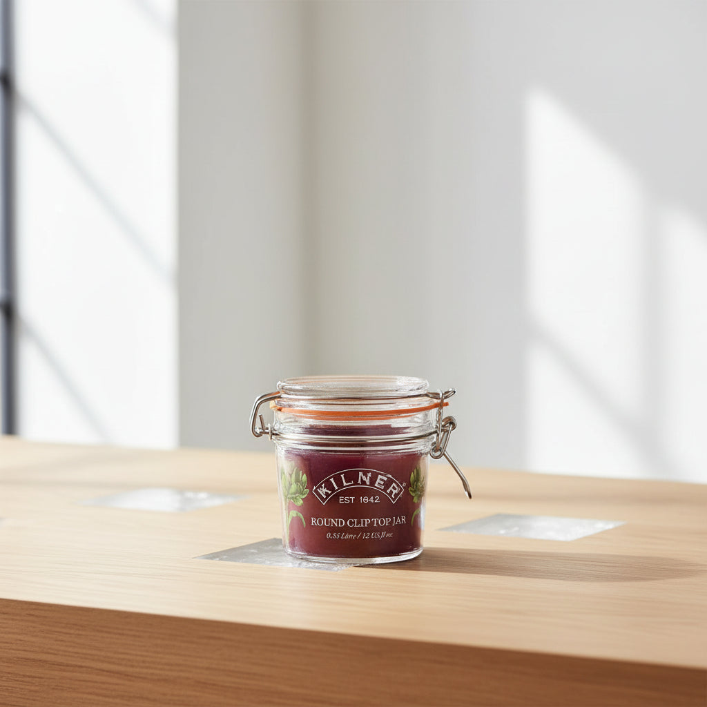 A Kilner round clip-top jar candle with a clear glass jar, metal wire bail, and orange rubber seal, filled with deep burgundy wax. The front label features the Kilner brand name and scent name 'Round Clip Top Jar'.