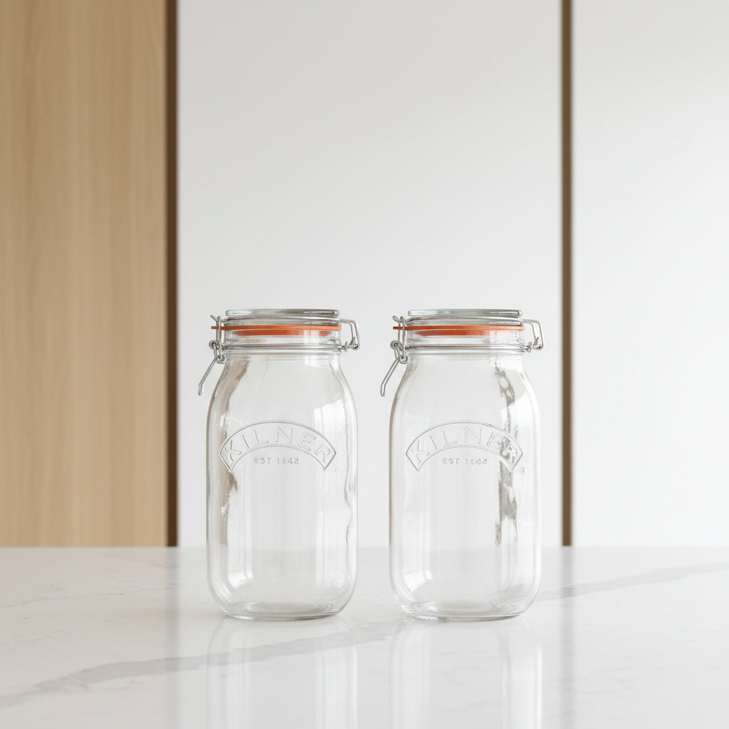 Two clear Kilner glass mason jars with wire bail lids and orange rubber gaskets, shown side by side on a white background.