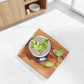 Green leafy vegetables on a digital kitchen scale with a wooden cutting board.