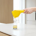 Yellow lemon squeezer being used to extract juice into a glass on a white background