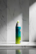 A single aerosol spray can shown upright against a solid black background. The can has a white pointed top, a bright yellow-green nozzle, and a printed label that fades vertically from teal/blue at the top to green and yellow at the bottom.