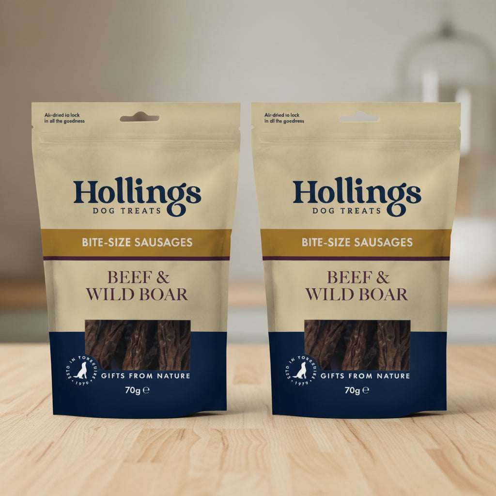 A 70g bag of Hollings Dog Treats Beef & Wild Boar Bite-Size Sausages. The packaging is beige and navy blue with a clear window showing the dark brown meat inside.