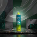 Tigi Bed Head Master Piece Hair Spray can in a teal-to-yellow gradient design with a lime green spray top, shown alongside a clear plastic cap on a white background.