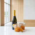 Bottle of champagne with two jars of orange marmalade on a wooden surface.