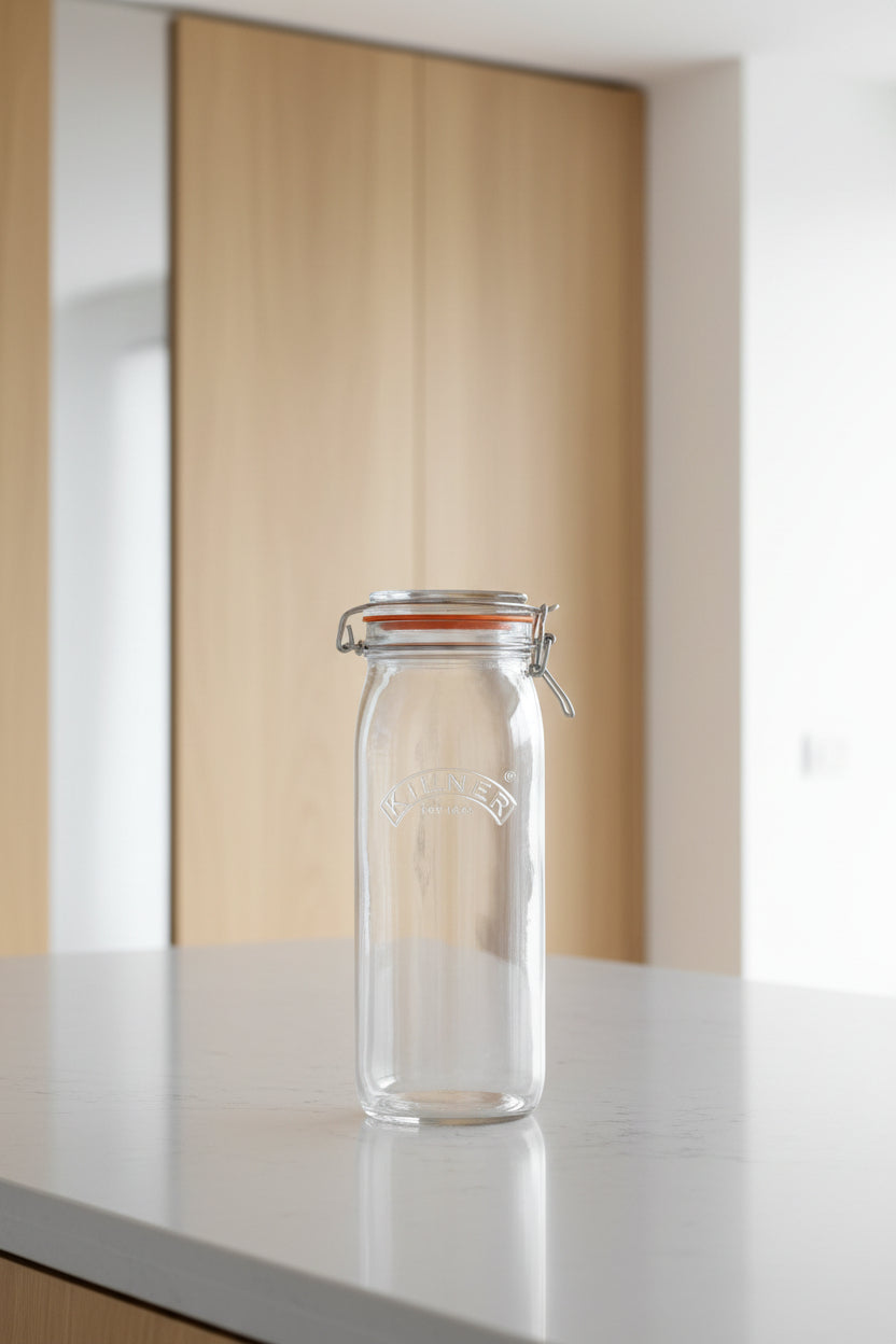 A clear glass Kilner jar with a metal clamp lid and an orange rubber gasket, shown on a plain white background.