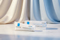 Two white cosmetic pouches and one white carton of La Roche-Posay Cicaplast Baume B5+ shown on a plain white background. The packaging features blue and light blue branding and text.