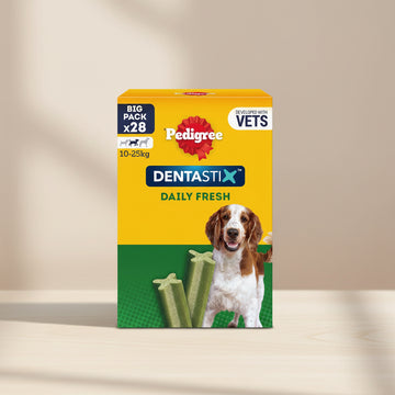 A box of Pedigree Dentastix Daily Fresh dog treats, designed for dogs weighing 10-25kg. The packaging is bright yellow on top and green on the bottom, featuring the red Pedigree logo, the blue Dentastix brand name, and an illustration of a brown and white dog alongside two green star-shaped treats.