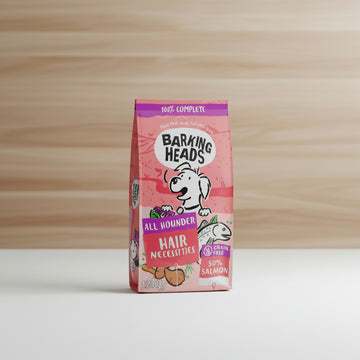 A 12kg bag of Barking Heads All Hounder Hair Necessities dog food, featuring a pink and red design with a cartoon dog and illustrations of salmon and carrots.
