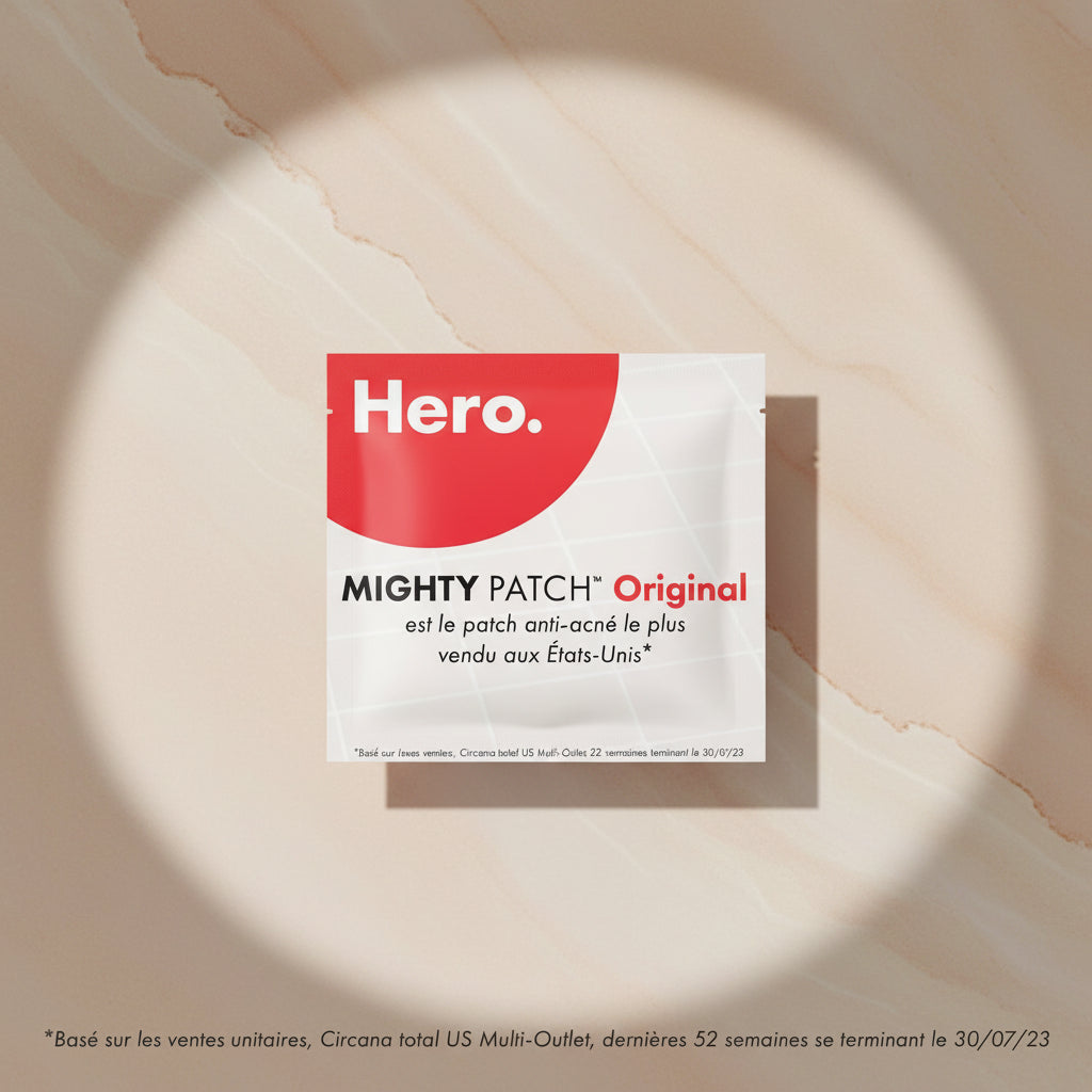 Promotional graphic for Mighty Patch Original anti-acne patch, featuring a large red circle with the white word 'Hero.' and French text on a light off-white grid background.
