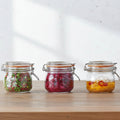 Three glass jars with metal clamps on a wooden surface, containing various contents.