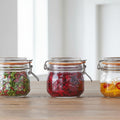 Three glass jars with metal clamps on a wooden surface, containing various contents.