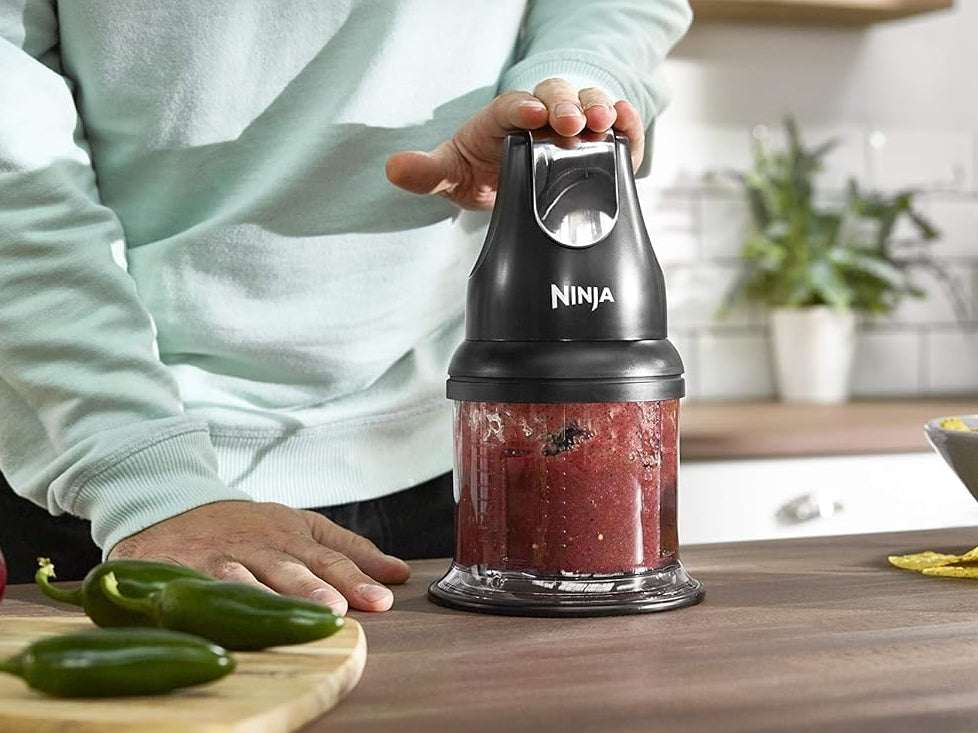Person using a Ninja food chopper on a kitchen counter with ingredients around