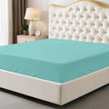Teal fitted sheet on a bed with a decorative headboard and nightstand.