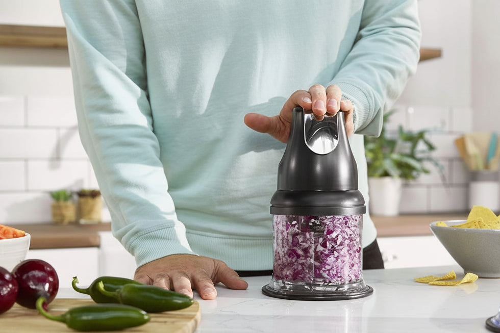 Person using a Ninja food chopper on a kitchen counter with vegetables around