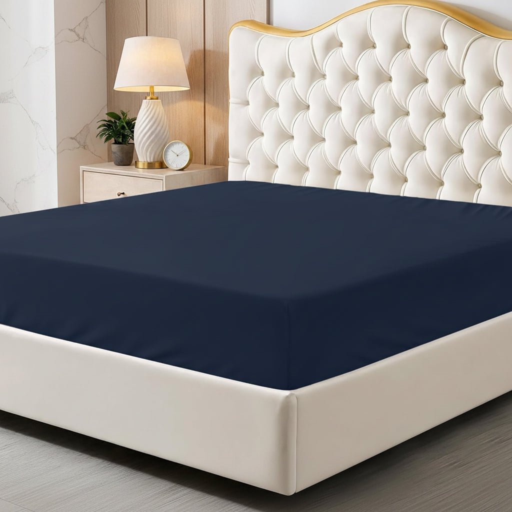 Navy blue fitted sheet on a bed with a decorative headboard and nightstand.
