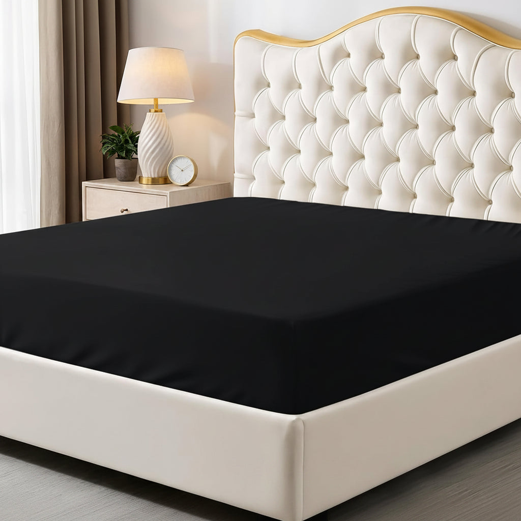 Black fitted sheet on a bed with a decorative headboard and nightstand in a bedroom setting.