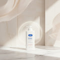 Person applying lotion to their leg with a bottle labeled 'E45' on a neutral background.
