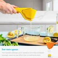 Yellow lemon squeezer being used to extract juice into a glass pitcher with lemons and mint leaves on a cutting board.