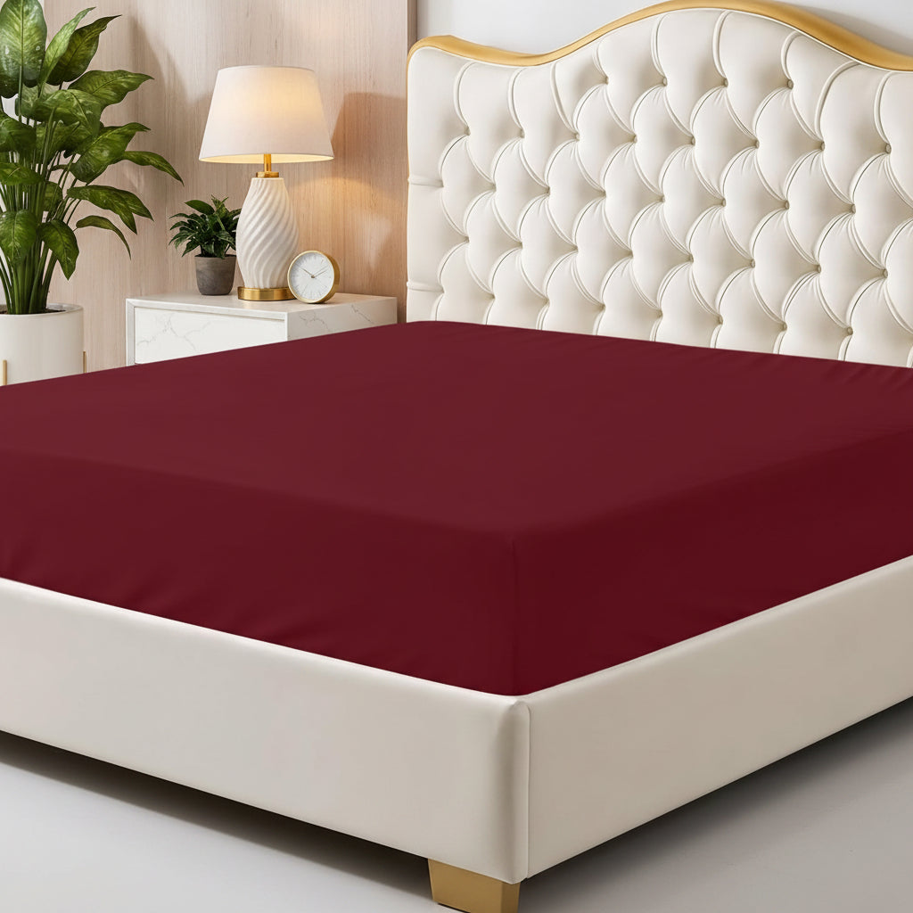Maroon fitted sheet on a bed with a decorative headboard and nightstand.