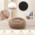 A plush round pet bed in taupe-brown faux fur is shown on a white background with four circular inset detail photos and feature icons. The insets show the fluffy white filling, a close-up of the brown faux fur, a close-up of the non-slip textured bottom, and a folded bed being washed in a machine.