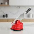 A red Any Sharp knife sharpening device with a black base, shown with a stainless steel kitchen knife being sharpened by a hand against a white background.