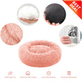 A plush round pet bed in light pink faux fur, shown on a white background with feature callout circles and icons. The main product is the pink bed, surrounded by circular insets showing fluffy white faux fur, a black textured non-slip pad, soft fabric texture, and a hand washing the bed in a washing machine.