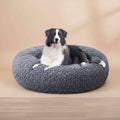 A black and white dog lying on a round, fluffy gray pet bed against a plain white background.