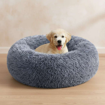 A golden retriever puppy sitting inside a round, fluffy gray dog bed on a white background.