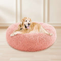 A golden retriever dog lying on a round, fluffy pink pet bed against a plain white background.