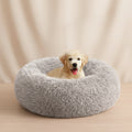 A light golden retriever puppy sitting inside a round, fluffy light gray pet bed on a white background.