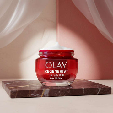 Olay Regenerist Ultra Rich Day Cream in a red jar with a white cream scoop on top, on a white background.