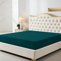 Teal fitted sheet on a bed with a decorative headboard and nightstand in a bedroom setting.