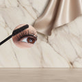 Close-up of an eye with long, thick eyelashes being applied with a mascara wand.