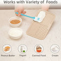 Beige mat with textured surface, blue spatula, and bowls of peanut butter, yogurt, canned food, and cream on a light gray background.