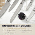 A set of kitchen knives with silver blades and handles arranged diagonally on a white marble surface, with a black circular knife sharpener placed in the center. Text below reads 'Effortlessly Restore Dull Blades' and lists knife types the sharpener can fix.