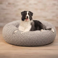 A black and white dog lying on a round, fluffy gray pet bed against a plain white background.