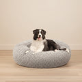 A black and white dog lying on a round, fluffy gray pet bed against a plain white background.