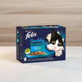 A box of Purina Felix Doubly Delicious wet cat food, Fish Selection in Jelly, featuring a black and white cat peeking out of the packaging on a dark blue background.