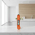 A woman in a kitchen uses an orange digital food thermometer to check the temperature of a pot on a gas stove. The image includes a text overlay that reads 'LOCK TEMPERATURE' and 'Lock the Temp to View the Reading Away From the Heat'.
