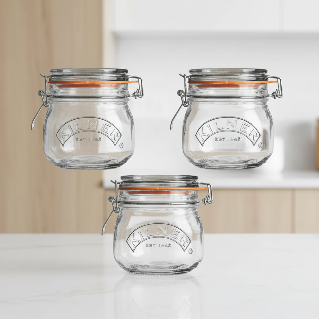 Three clear Kilner glass jar lids with metal wire hinged clasps and orange rubber gaskets, shown on a plain white background.