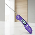 Purple digital multi-probe meat thermometer with rotating probes, shown with promotional text and graphics on a blurred grill background.
