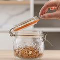 Glass jar with metal clasp lid filled with almonds, being opened by a hand.