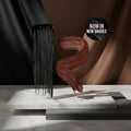 A hair color swatch graphic showing a thick black swatch on the left and a brown swatch on the right, with a circular badge reading 'NOW IN NEW SHADES' on a white background.