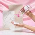 Garnier Micellar Water in a clear bottle with pink liquid, being poured onto a reusable white pad held in two hands against a light pink background, with a text panel explaining the three-step cleansing process.